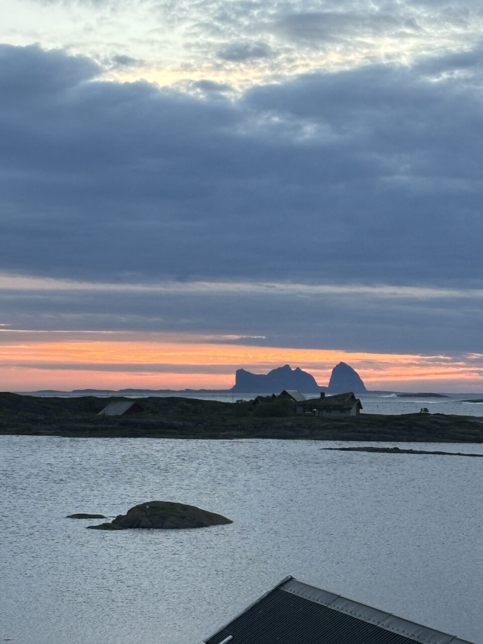 Øy med høye fjelltopper i solnedgang. Foto